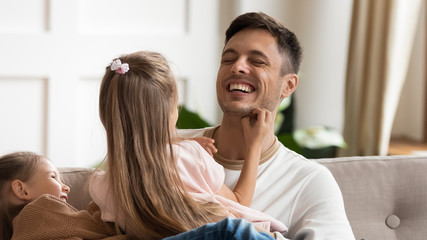 Head shot laughing young father having fun with happy playful little daughters. Joyful single dad...