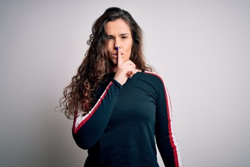 Young beautiful woman with curly hair wearing casual sweater over isolated white background asking to be quiet with finger on lips. Silence and secret concept.