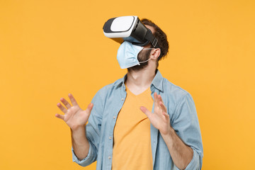 Young man in sterile face mask posing isolated on yellow wall background studio portrait. Epidemic pandemic coronavirus 2019-ncov sars covid-19 flu virus concept. Watching in headset spreading hands.