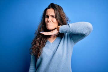 Young beautiful woman with curly hair wearing blue casual sweater over isolated background cutting...