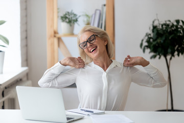 Happy 60 years old businesswoman with hands behind head relaxing in comfortable office chair during...