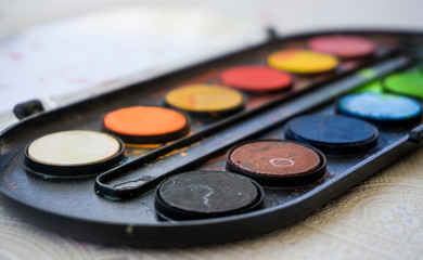 Obraz na płótnie Canvas Colors on watercolor palette closeup. Selective focus. Black, blue, brown, red, yellow, green, orange colors on palette.