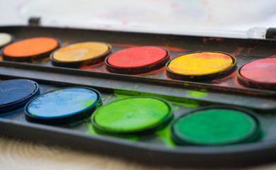 Colors on watercolor palette closeup. Selective focus. Black, blue, brown, red, yellow, green,...