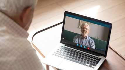 80s old man sit indoor look at pc screen talk with 50s male friend by video call. Multi-generational relatives communicating use modern tech internet connection laptop and videoconference application