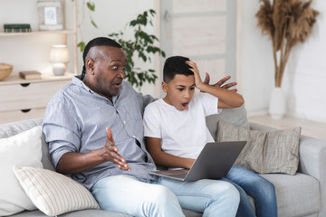 Obraz premium Black man and his grandson looking at laptop screen with shock