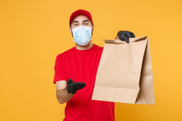 Fototapeta na wymiar Delivery man employee in red cap blank t-shirt uniform mask glove hold craft paper packet with food isolated on yellow background studio Service quarantine pandemic coronavirus virus 2019-ncov concept