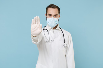 Male doctor man in white medical gown sterile face mask gloves isolated on blue background. Epidemic pandemic coronavirus 2019-ncov sars covid-19 flu virus concept. Showing stop gesture with palm.