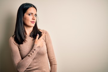 Obraz premium Young brunette woman with blue eyes wearing casual sweater over isolated white background Pointing with hand finger to the side showing advertisement, serious and calm face