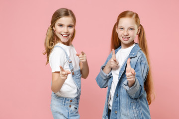 Smiling little kids girls 12-13 years old in white t-shirt, denim clothes isolated on pink background children portrait. Childhood lifestyle concept. Mock up copy space. Point index fingers on camera.