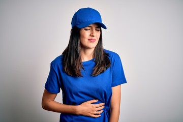 Young delivery woman with blue eyes wearing cap standing over blue background with hand on stomach because indigestion, painful illness feeling unwell. Ache concept.