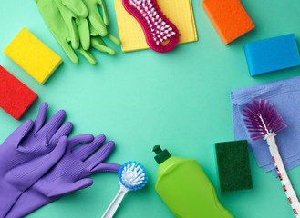 rubber gloves for cleaning, multi-colored sponges, brushes and cleaning fluid in a green plastic bottle on a green background