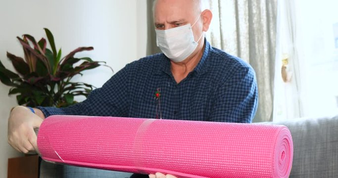 Paris, France - March 2020: handheld footage senior male wearing plastic protective gloves and surgical medical respiratory mask during worldwide coronavirus confinement unboxing yoga mat