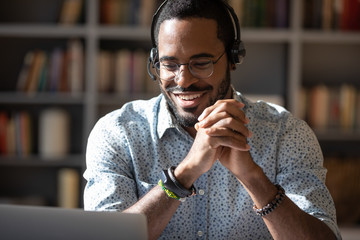 Smiling African American man in headset watch webinar or training on modern computer, happy...