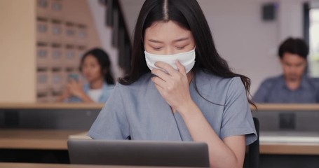 Asian young woman using computer laptop for work at office. She wearing protection mask coughing be congested with virus infection, coronavirus infection in city. Health care and medical concept - Powered by Adobe
