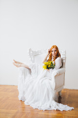Fototapeta na wymiar Portrait of a red-haired beautiful girl with a Mimosa in a long white dress
