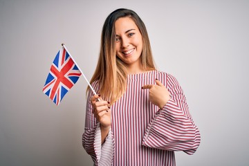 Young beautiful blonde woman with blue eyes holding united kingdom flag with surprise face pointing finger to himself