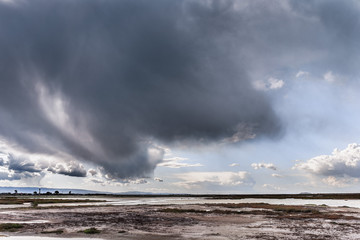Dark storm cloud bringing rain in South San Francisco bay; Tidal ponds and marsh land visible under the clouds; Don Edwards National Wildlife Refuge, San Jose, California