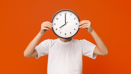 Teen boy covering his face with big clock, orange panorama