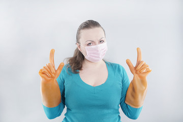 Fototapeta premium a middle-aged housewife wears a protective medical mask and large rubber gloves for sterility on a white background. a woman in a home sweater is ready to clean the house in quarantine