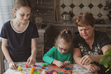 Obraz premium An adult woman and two little girls make plasticine figurines at home. Grandmother and granddaughters are sitting at home. Family Values Concept