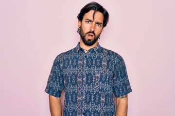 Young handsome hispanic bohemian man wearing hippie style over pink background In shock face, looking skeptical and sarcastic, surprised with open mouth