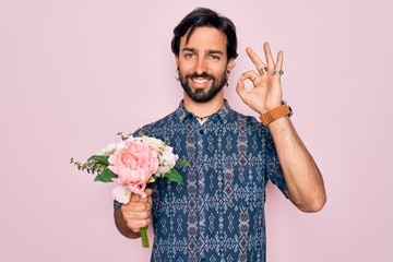 Young handsome hispanic bohemian hipster man with bear holding flowers bouquet doing ok sign with fingers, excellent symbol