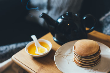 Pancakes with honey on wooden tray in cozy room.