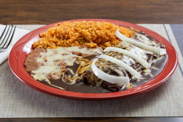A view of a Mexican plate of mole enchiladas, in a restaurant or kitchen setting.
