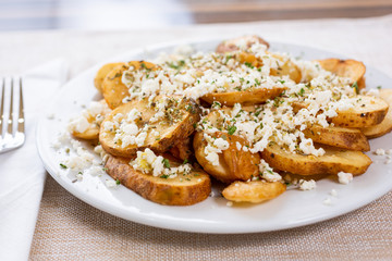 A view of a plate of potato slices and feta cheese, in a restaurant or kitchen setting. 