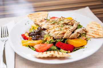 A view of a plate of Mediterranean style chicken salad with fruit and pita bread, in a restaurant or kitchen setting.