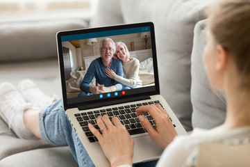 Fototapeta na wymiar Over girl shoulder pc screen view, sit on sofa living in country grandparents communicating with adult granddaughter via videocall. Parents and grownup daughter talking use videoconference app concept