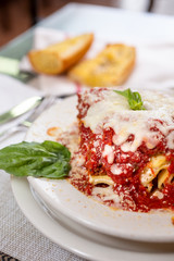 A view of a plate of cheesy lasagna and a side of garlic bread, in a restaurant or kitchen setting.