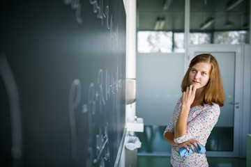 Fototapeta na wymiar Pretty, young female student in front of a blackboard during math class
