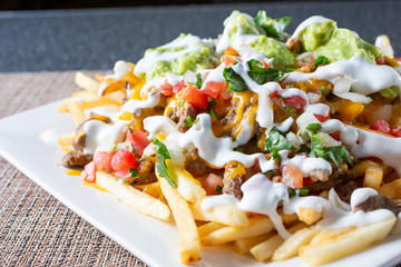 A closeup view of a plate of carne asada fries, in a restaurant or kitchen setting.