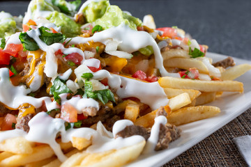 A closeup view of a plate of carne asada fries, in a restaurant or kitchen setting.