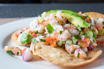 A closeup view of a plate of shrimp tostada, in a restaurant or kitchen setting.