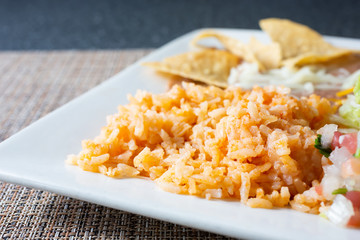 A closeup view of a serving of Mexican rice on a plate, in a restaurant or kitchen setting.