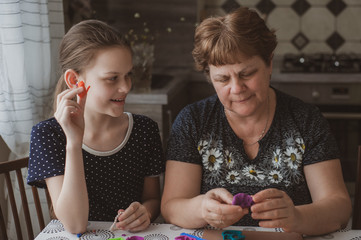 Fototapeta premium Adult woman and teenage girl make plasticine figurines at home. Grandmother and granddaughter are sitting at home. Family Values Concept
