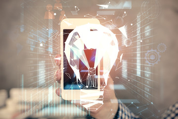 Double exposure of man's hands holding and using a digital device and bulb hologram drawing. Idea concept.
