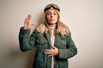 Young brunette skier woman wearing snow clothes and ski goggles over white background Swearing with hand on chest and open palm, making a loyalty promise oath