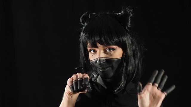 girl on a black background with black make-up hair and fingers, shows how to grab a torn pipe with her hands and looks at the camera