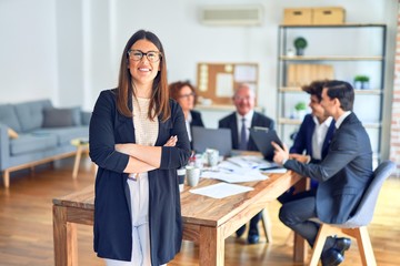 Group of business workers smiling happy and confident working together in a meeting. One of them, standing with smile on face looking at camera at the office.