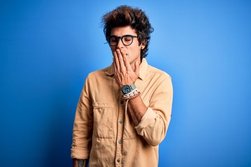 Young handsome man wearing casual shirt standing over isolated blue background bored yawning tired covering mouth with hand. Restless and sleepiness.