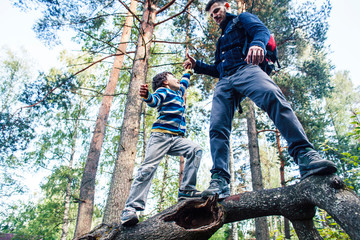 little son with father climbing on tree together in forest, lifestyle people concept, happy smiling family on summer vacations