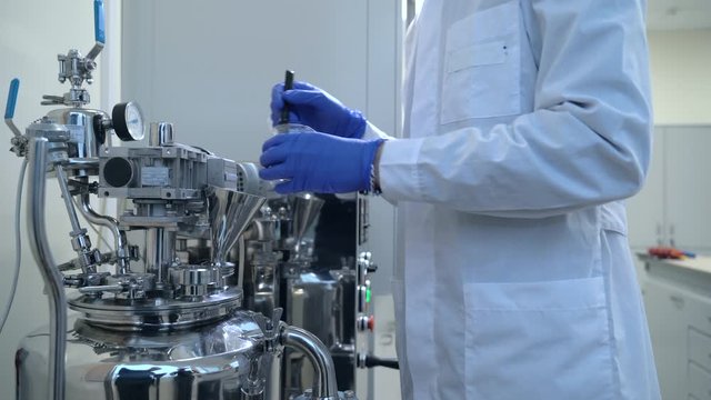 Man employee is working with equipment and chemicals in modern pharmaceutical laboratory spbas. Male chemist pours white powder into compartment of metal facilities standing in factory workshop