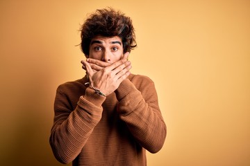 Young handsome man wearing casual shirt and sweater over isolated yellow background shocked covering mouth with hands for mistake. Secret concept.