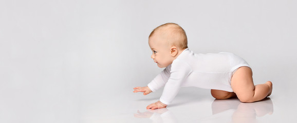 Chubby ginger baby boy in bodysuit, barefoot. He smiling, creeping on floor isolated on white background. Close up, copy space - obrazy, fototapety, plakaty