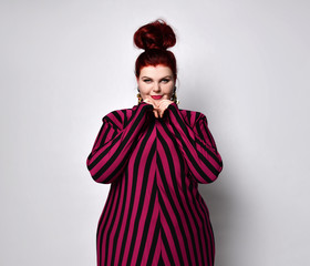 large red-haired model with a bun-shaped hairstyle, a dark pink tight-fitting striped dress and...