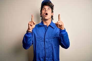 Young mechanic man wearing blue cap and uniform standing over isolated white background amazed and...