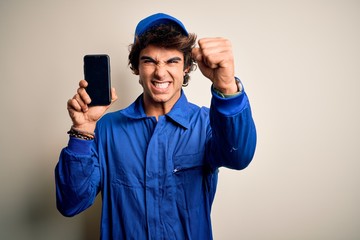 Young mechanic man wearing uniform holding smartphone over isolated white background annoyed and frustrated shouting with anger, crazy and yelling with raised hand, anger concept